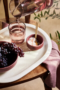 Crop person pouring water into glass placed on tray with grapes