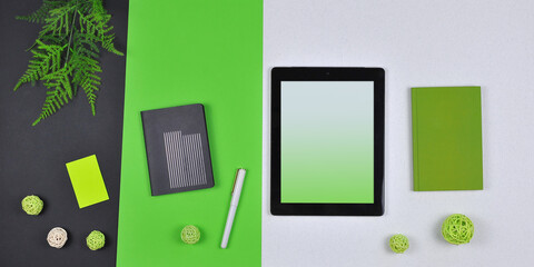 Digital tablet mockup, green and black notebooks ,pen , paper sticker, green fern leaves, rattan balls isolated on black- lime- white melange background. Top view ,flat lay. Free copy space