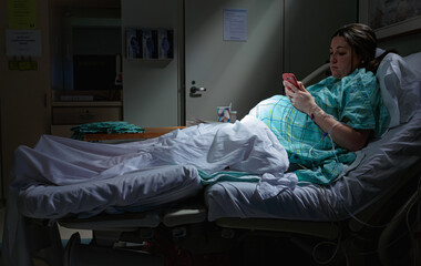 Pregnant woman on cell smart phone in labor laying in hospital bed with rays of light on belly...