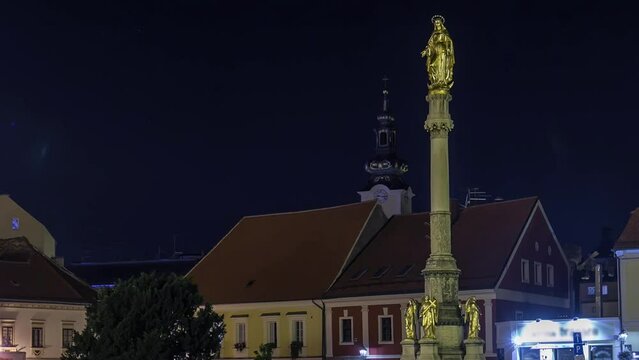 Holy Mary monument in front of the Cathedral illuminated at night timelapse in Zagreb, Croatia. Historic buildings on the background