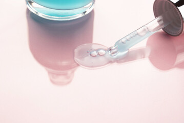 Pipette with a cosmetic product on a pink background. Cosmetic bottle with blue liquid. Copy space