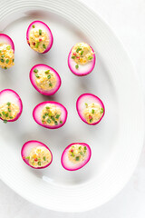 Top down view of a platter of beet juice dyed Deviled eggs, ready for eating.