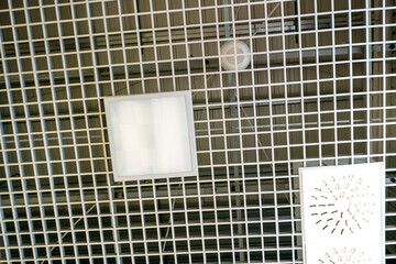 Various lighting fixtures and air conditioning grilles on the ceiling of the restaurant. LED lamps on the suspended mesh ceiling. Industrial air conditioning in the large hall.
