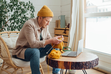Middle aged man knitting at home. Knitting project in progress. Man learning a new hobby - 572030222