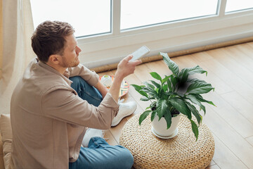 Man taking smartphone picture of plant at home. Housework and care plant concept