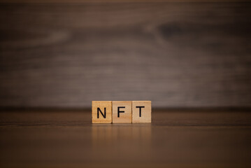 The word NFT is made up of wooden cubes tablets on a dark wooden background