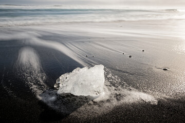 small ice block on black sand beach in Iceland with blurred water