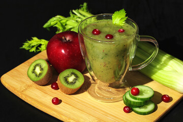 Fototapeta na wymiar Fresh green smoothie in a glass cup with celery, apple, cucumber, kiwi and cranberries, healthy vegan drink.