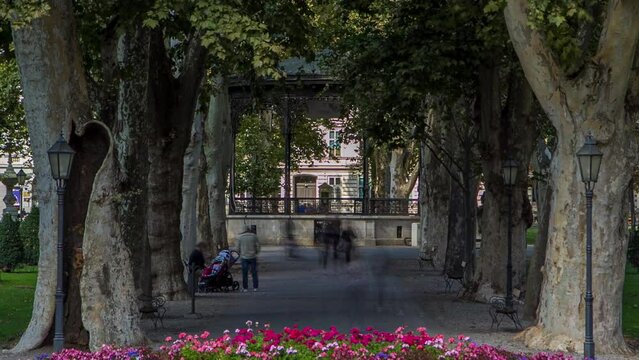 People walking around pavillion in Zrinjevac park timelapse in Zagreb, Croatia. Zrinjevac is spread over 12540 sq meters in city center. Flowerbed on foreground