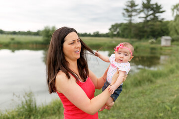 Infant baby girl pulling mother's hair while being held outdoors at lake