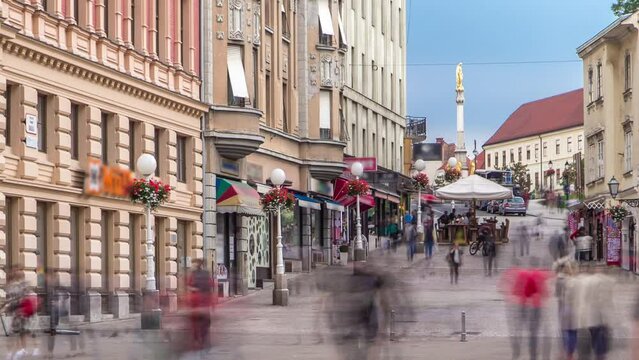 Street with historic buildings in downtown and Holy Mary monument in front of the Cathedral on the background timelapse in Zagreb, Croatia. People walking around