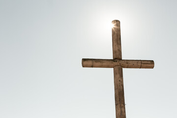 Sun shining on brown rustic wooden cross against sky