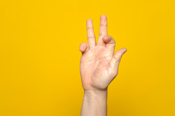 Tough man's hand making a strange and complicated gesture with his hand. It can represent a surfer, gippie or meditation gesture isolated on yellow background.