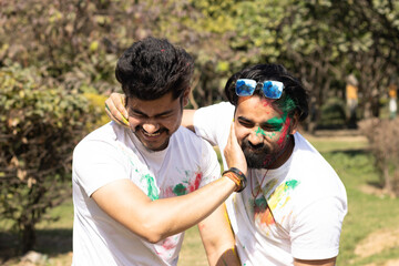 Two young boys friends family celebrating enjoying holi festival of colors colours with gulal abeer color powder outdoor in a park, a popular hindu festival celebrated across india