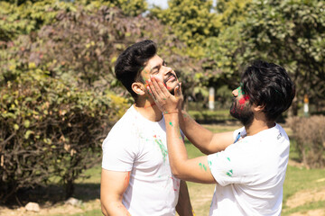 Two young boys friends family celebrating enjoying holi festival of colors colours with gulal abeer color powder outdoor in a park, a popular hindu festival celebrated across india