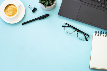 Office workspace with laptop, headphones, notepad and coffee cup. Flat lay image on blue with copy space.