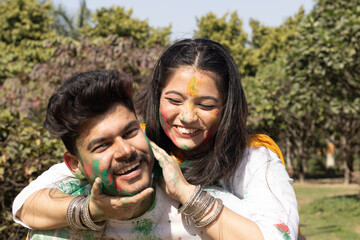 Fototapeta premium A young couple friends family boy girl man woman celebrating enjoying holi festival of colors colours with gulal abeer color powder outdoor in a park, a popular hindu festival celebrated across india