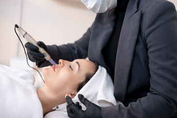 beautician hands in sterile gloves using dermapen during skincare procedure. Young woman receiving...