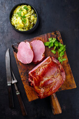 Traditionell geschmortes badisches Schäufele mit Kartoffelsalat und Petersilie aufgeschnitten als Draufsicht auf einem rustikalen Holz Schneidebrett 