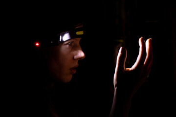 A girl with a headlamp shines in the dark, the light of a lantern on her head
