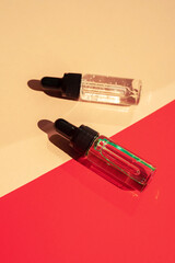 Two glass bottles with cosmetic liquid on bright red background with shadows and light reflections.