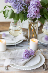 Obraz na płótnie Canvas Beautiful table decor for a wedding dinner with a spring blooming lilac flowers. Celebration of a special holiday marriage event. Fancy white plates, wineglasses, candles. Countryside style