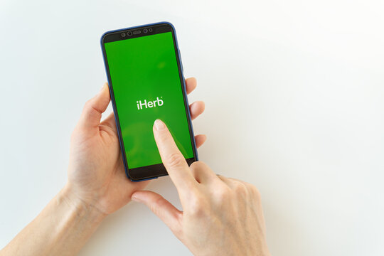 Kyiv, Ukraine - December 13, 2022: Woman hand holding phone iPhone with Internet store iHerb app with logo on the screen