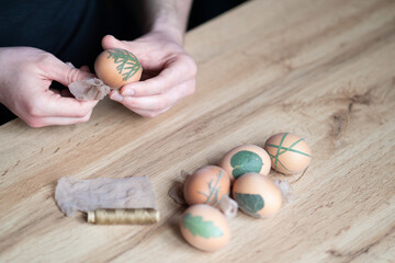 close up of male hands decorating easter eggs with different types of leaves. Interesting method for decorating easter eggs with leaves. Eggs decoration with leafs. Young man decorating easter eggs.