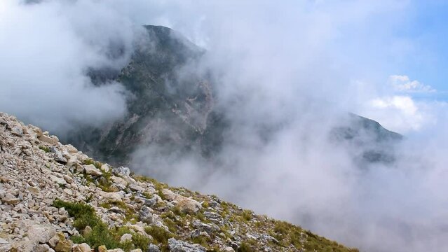 White fog slowly creeps up the high mountain. View from the highlands. A blue sunny sky is visible through the fog. Travel in Albania. Road to Llogara Pass.