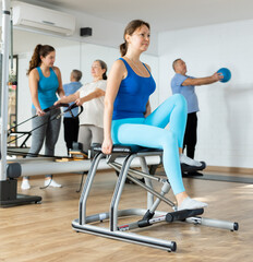 Sportive middle-aged woman doing pilates exercises on pedal pilates chair in fitness studio during...