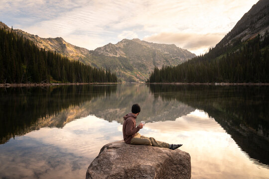 Hiker drinking coffee at alpine lake in Montana on a backpacking trip