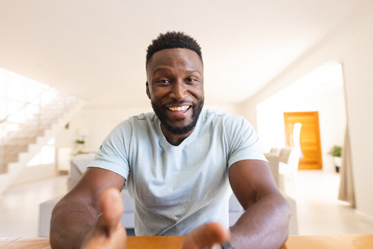 Happy african american man sitting at table and having video call