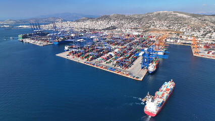 Aerial drone photo of huge fully loaded container tanker ship reaching with help of tug boat logistics and container terminal of Perama, Attica, Greece - obrazy, fototapety, plakaty