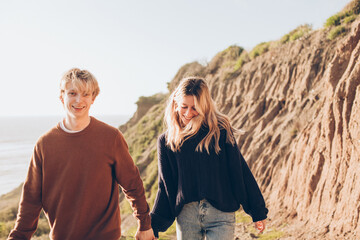 couple walking on the path on the bluff over the ocean on beach holding hands and smiling