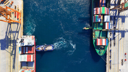 Aerial drone top down photo of container ship guided by tug boat to logistics terminal