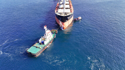 Aerial drone photo of huge fully loaded container tanker ship reaching with help of tug boat...