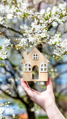 The girl holds the house symbol against the background of blossoming cherry
