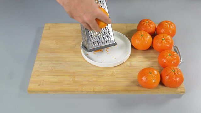A man rubs the peel of a mandarin citrus on a grater. Folds the zest. High quality 4k footage