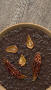 Frijoles refritos with roasted garlic and dried roasted chili on top. Table spin. Seamless loop. Vertical video.