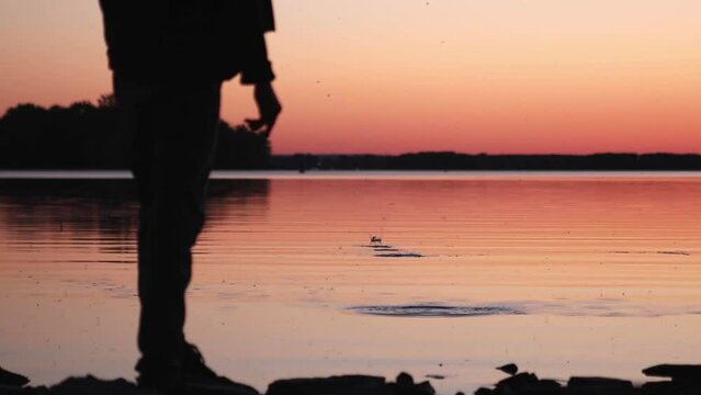Man skipping a stone across a sill lake at sunset in slow motion.