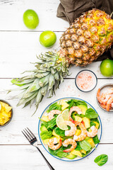 Fresh pineapple salad with shrimps, spinach, avocado and lime on white kitchen table, top view. Healthy eating, balanced, clean diet food, weight loss concept