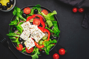 Vegetable greek salad with feta cheese, olives, tomatoes, paprika, cucumber and red onion, healthy mediterranean food, low calories eating. Black table background, top view