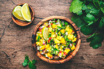 Spicy mango salsa sauce with red chili peppers, onion, garlic lime and cilantro, rustic wooden...