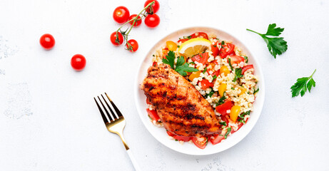 Grilled chicken breast fillet with tabbouleh salad with bulgur, tomato and parsley with lemon dressing, white table background, top view