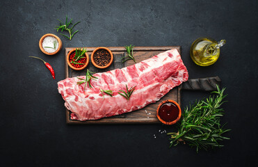 Raw pork ribs with rosemary and spices on rustic wooden cutting board prepared for cooking on black...