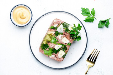 Aspic meat, cold boiled beef in spiced jelly broth on plate, dijon mustard dressing. White kitchen table background, top view