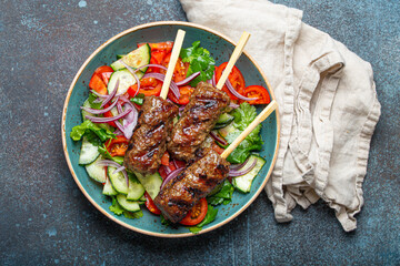 Grilled skewer meat beef kebabs on sticks served with fresh vegetables salad on plate on rustic...