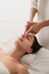 Crop masseuse massaging nose of client