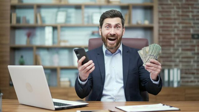 Overjoyed happy mature business man investor receive message with great news at desk in office Successful entrepreneur holding money and rejoices at good earnings income salary investment at workplace