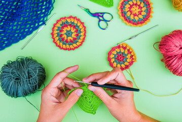 Close view of crocheting hands with blurred crochet motifs, hook